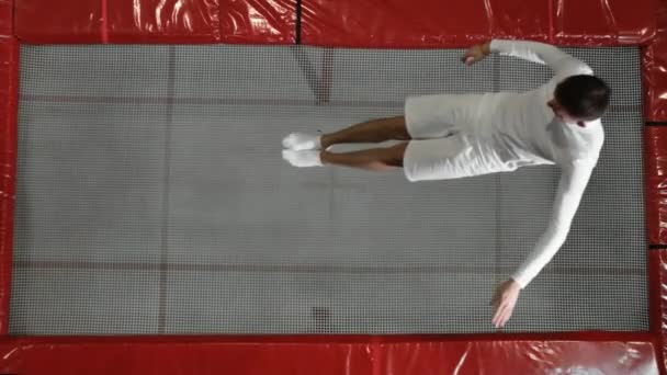 La vista desde el acróbata gimnasta superior vestido de blanco realiza una voltereta en el trampolín — Vídeo de stock