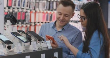 Modern elektronik mağazasında akıllı telefonlar ile vitrin yakın ayakta evli bir çift ve yeni bir akıllı telefon seçin. Cep telefonu satın al.