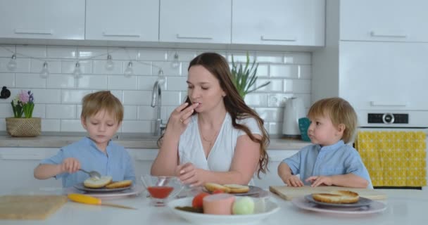 Mamá con dos hijos en la cocina en la mesa preparando hamburguesa para el almuerzo — Vídeo de stock