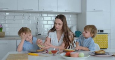 Mutfakta iki genç oğulları ile Genç Anne masada burger hazırlamak için öğle yemeği