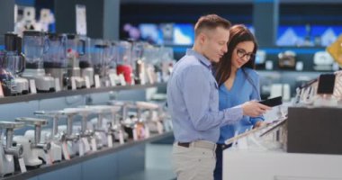 Genç güzel evli çift ekran dokunmatik kontrol bir elektronik mağaza akıllı telefonlar ile bir vitrin etrafında bir smartphone ayakta tutan bir gömlek ve gözlük bir kadın bir adam