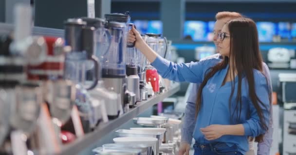 Joven pareja hombre y mujer en la tienda de electrodomésticos selecciona una licuadora para su cocina — Vídeo de stock