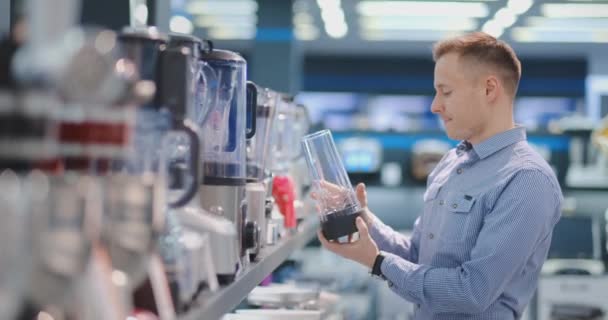 Im Gerätehaus wählt ein Mann im Hemd einen Mixer, um ihn zu kaufen, indem er das Gerät ansieht und hält. — Stockvideo