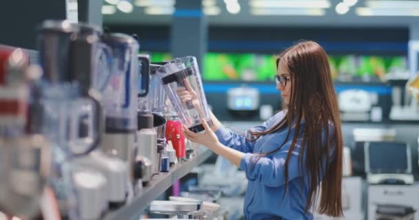 Na loja de eletrodomésticos, uma mulher morena de camisa escolhe um liquidificador para fazer compras, visualizando e segurando o dispositivo em suas mãos. . — Vídeo de Stock