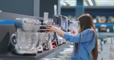 Aletleri mağazasında, bir gömlek esmer kadın inceleyen ve elinde cihazı tutarak alışveriş için bir blender seçer.