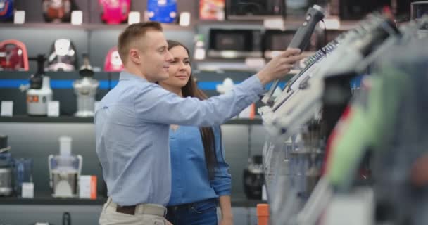 Na loja de eletrodomésticos, um casal feliz, um homem e uma mulher de roupas casuais, escolhem um liquidificador para fazer compras, visualizando e segurando o dispositivo em suas mãos. . — Vídeo de Stock