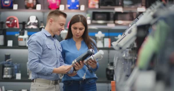 Na loja de eletrodomésticos, um casal em roupas cotidianas escolhe um liquidificador para a compra, visualizando e segurando o dispositivo em suas mãos. . — Vídeo de Stock