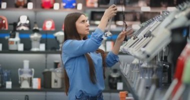 Aletleri mağaza mutfak aletleri, mavi bir gömlek bir esmer kadın elinde bir blender seçer ve tasarım ve özellikleri dikkate.