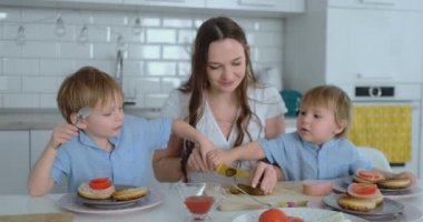 Hamburger ile beyaz ışık Kunası yemek iki çocuk oğulları ile güzel genç anne