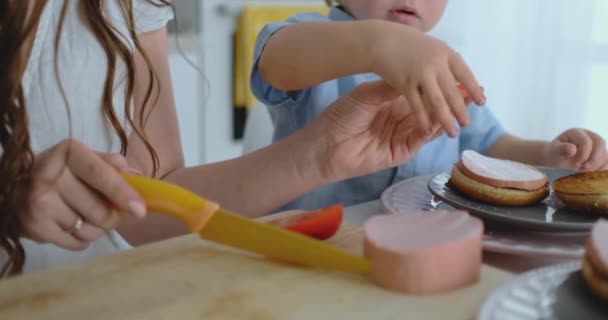 Mladá matka s malým dítětem společně nakrájí nůž a rajče na domácí Burger. Jídlo v zdravých potravinách — Stock video