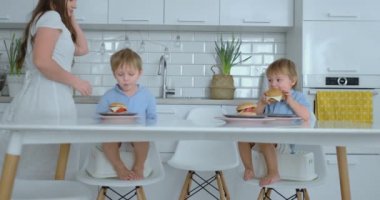 Mavi gömleklere sahip iki çocuk parlak mutfakta Hamburger yiyor.