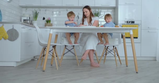 テーブルのキッチンで2人の子供を持つお母さんは、昼食のためにハンバーガーを準備します — ストック動画