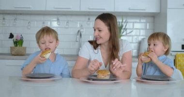 İki genç oğulları ile anne evde Hamburger yiyor