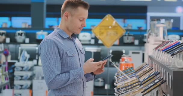 O homem escolhe entre dois telefones no balcão um smartphone mais poderoso e moderno para negócios. Comprar Dispositivos Portáteis para Negócios — Vídeo de Stock