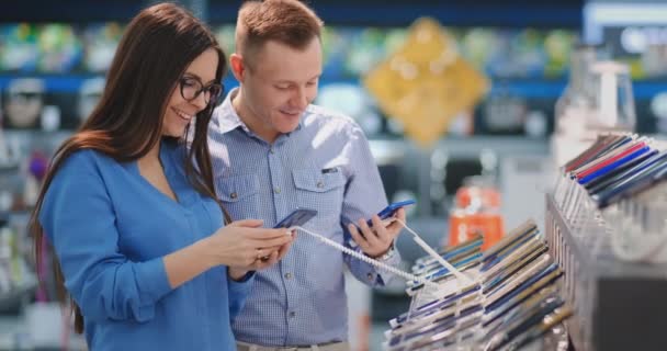 Der Mann hält sein Smartphone in der Hand und zeigt auf ein anderes Handy, das in Frauenhand ist. Innenausstattung eines Tech-Stores. — Stockvideo