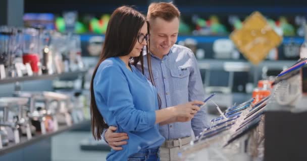 Счастливая пара смотрит на новую цифровую камеру в магазине электроники — стоковое видео