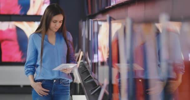 Cliente feminino moderno inteligente escolhendo grandes aparelhos de TV na loja de eletrônicos. Novas gerações de ecrãs . — Vídeo de Stock