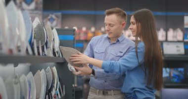 Genç evli çift, hırdavatçıda yeni bir ev almak için ütü seçiyor.