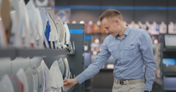 Jonge knappe man op zoek naar ijzer te kopen in een winkel van elektrische apparaten — Stockvideo
