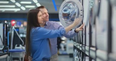 Güzel adam ve kadın yeni modern ev için tüketici elektroniği mağazasında modern akıllı çamaşır makinesi seçin.