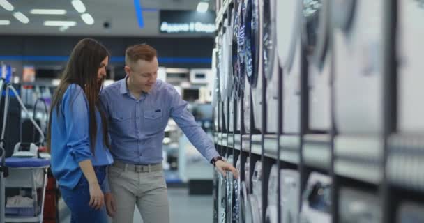 Young married couple man and woman in casual clothes appliances store choose to buy washing machine for home. Open the door looking into the drum, compare the design and characteristics of the devices — 비디오