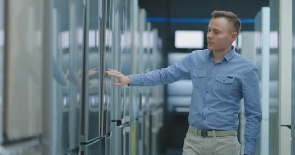 Un hombre abre la puerta de la lavadora inspeccionar el diseño y la calidad antes de comprar en una tienda de electrónica de consumo. Lea la información sobre el precio y las características — Vídeo de stock