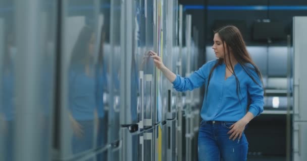 Joven morena sexy mujer en camisa para abrir la puerta del refrigerador en la tienda de electrodomésticos y comparar con otros modelos para comprar la nueva casa — Vídeos de Stock