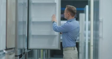 Adam aletleri mağazasında buzdolabının kapısını açmak ve yeni ev satın almak için diğer modeller ile karşılaştırmak