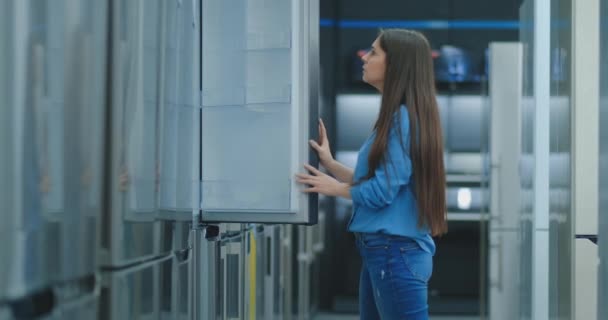 Una mujer joven para abrir la puerta del refrigerador para almacenar electrodomésticos y comparar con otros modelos para comprar la nueva casa — Vídeos de Stock