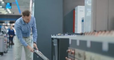 Gömlek Yakışıklı Adam mağazada bulaşık makinesi aletleri kapısını açmak ve yeni ev satın almak için diğer modeller ile karşılaştırmak