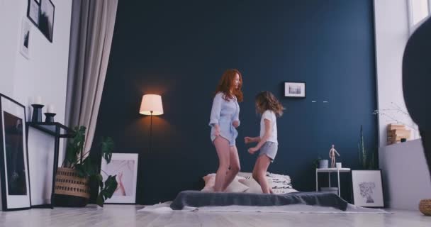 Glücklich niedliche Tochter und junge Mutter springen und tanzen auf dem Bett, während Spaß im Urlaub zu Hause haben — Stockvideo