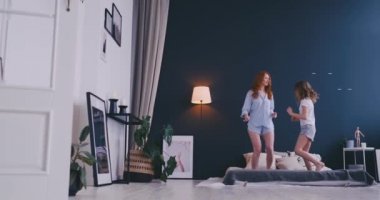 Sevimli küçük kız onun sevgi dolu bir anne ile modern tarzı birlikte atlama ve yatakta yüksek beş sabah sırasında evde rahat yatak odasında veren dans eğlenceli