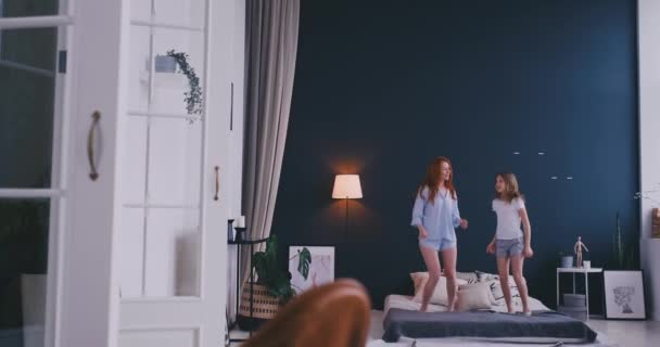 Feliz linda hija y madre joven saltando y bailando en la cama mientras se divierten durante las vacaciones en casa — Vídeo de stock