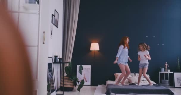 Divertente bambina con la sua amorevole madre divertirsi imparare la danza in stile moderno insieme a guardare lo spettacolo di danza in TV e saltare sul letto durante la mattina a casa — Video Stock