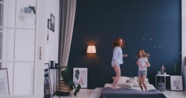 Sevimli küçük kız onun sevgi dolu bir anne ile modern tarzı birlikte atlama ve yatakta yüksek beş sabah sırasında evde rahat yatak odasında veren dans eğlenceli