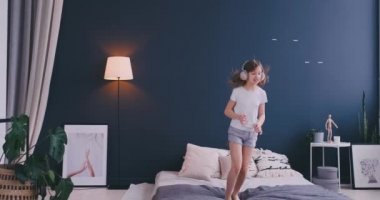 Sevimli küçük kız dans kablosuz kulaklık ile şarkı tarak ve eğlenceli tatil sabah evde yatakta ışık yatak üzerinde atlama