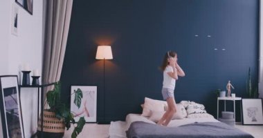 Litl kız yatakta dans ve kablosuz kulaklık ile müzik dinliyor. Boş zaman ve modern yaşam tarzı kavramı. Pijama kız sabah yatakta atlama ve gülümseyerek.