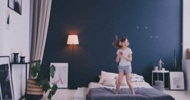 Kulaklık ile müzik dinlemek ve ebeveyn yatağında dans küçük bir kız portresi. Konsept: Müzik, özgürlük, mutluluk