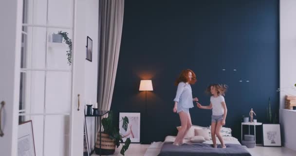 Heureuse famille de fille mignonne et jeune mère sautant et dansant sur le lit tout en s'amusant le matin pendant les vacances à la maison — Video