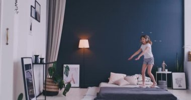 Litl kız yatakta dans ve kablosuz kulaklık ile müzik dinliyor. Boş zaman ve modern yaşam tarzı kavramı. Pijama kız sabah yatakta atlama ve gülümseyerek.