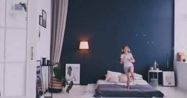 Mutlu küçük kız yatakta atlama kulaklıklar ile