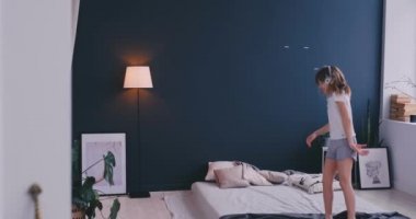 Litl kız yatakta dans ve kablosuz kulaklık ile müzik dinliyor. Boş zaman ve modern yaşam tarzı kavramı. Pijama kız sabah yatakta atlama ve gülümseyerek.