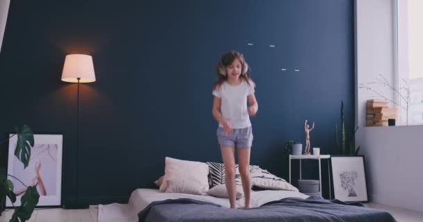 Retrato de una niña escuchando la música con los auriculares y bailando en la cama de sus padres. Concepto: Música, libertad, felicidad — Vídeo de stock