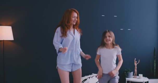 美しい母と娘は、自宅のベッドでジャンプしながら楽しみを抱えています。 — ストック動画