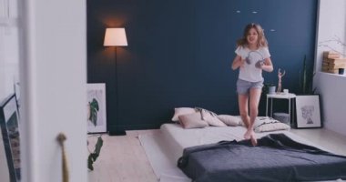 Litl kız yatakta dans ve kablosuz kulaklık ile müzik dinliyor. Boş zaman ve modern yaşam tarzı kavramı. Pijama kız sabah yatakta atlama ve gülümseyerek.