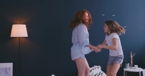 Gelukkig schattige dochter en jonge moeder springen en dansen op bed terwijl veel plezier tijdens de vakantie thuis — Stockvideo