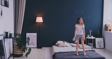 Sevimli küçük kız dans kablosuz kulaklık ile şarkı tarak ve eğlenceli tatil sabah evde yatakta ışık yatak üzerinde atlama