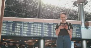 Skorbord-kalkış yakınında bir akıllı telefon ile havaalanında genç bir kadın