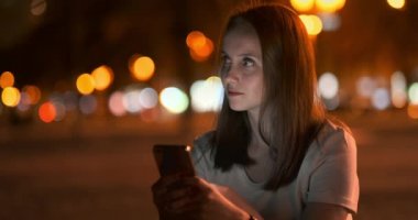 Geceleri, genç bir kız elinde bir akıllı telefon tutar ve ekrana bakar