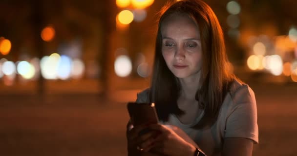 Jeune fille dans la ville de nuit écrit des messages texte dans un smartphone — Video